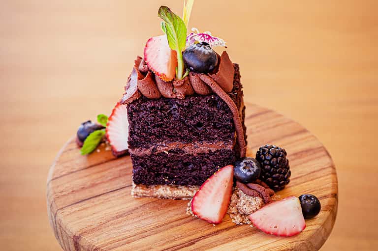 Decadent chocolate layer cake with berries and whipped cream on wooden serving board