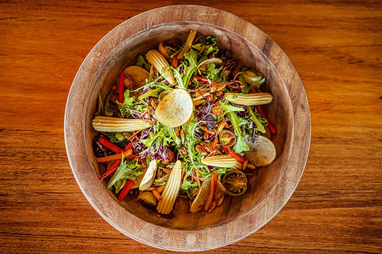 Colorful salad in wooden bowl with fresh vegetables and greens on wood table