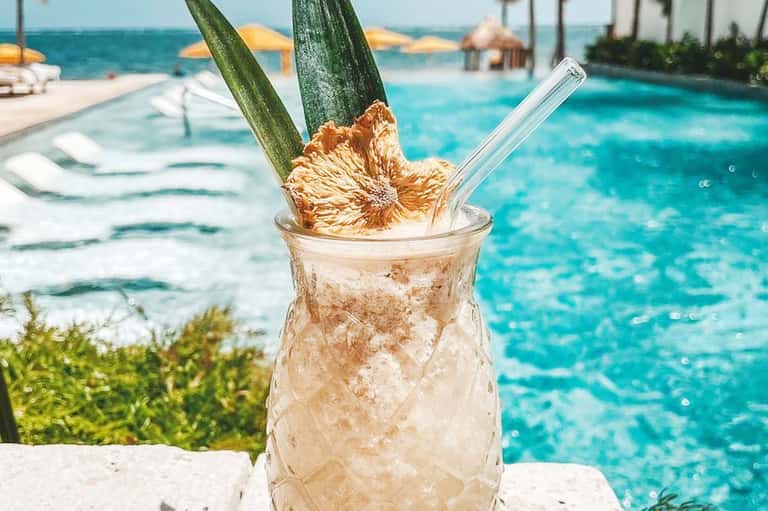 Tropical cocktail with pineapple garnish by turquoise pool and ocean