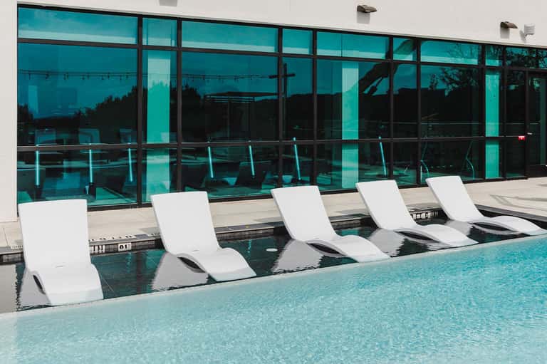 Indoor spa loungers submerged in pool water with large turquoise-tinted windows overlooking landscape