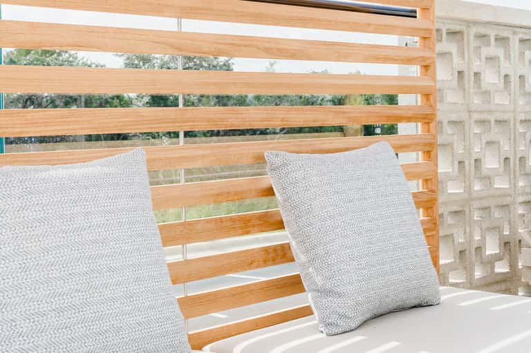 Modern wooden deck chair with gray herringbone pillows overlooking garden
