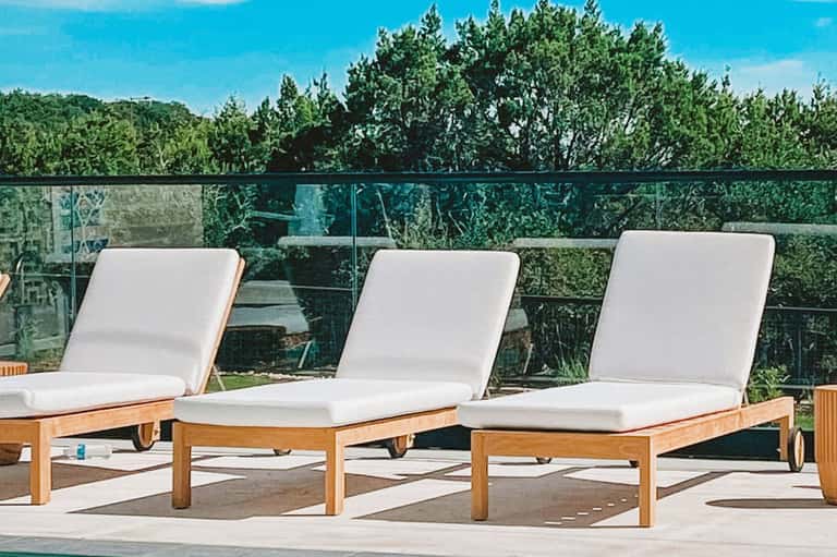 Three wooden lounge chairs with white cushions overlooking green landscape