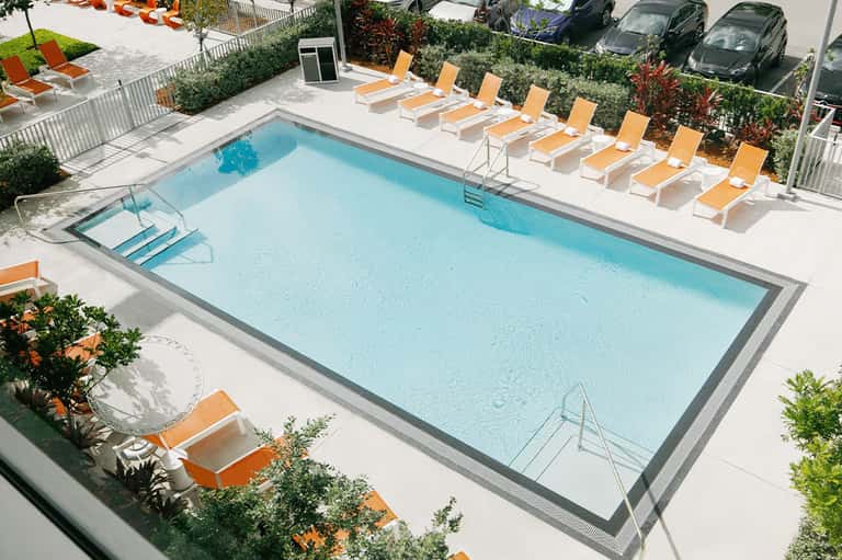 Aerial view of rectangular pool with orange lounge chairs and white umbrellas on concrete deck