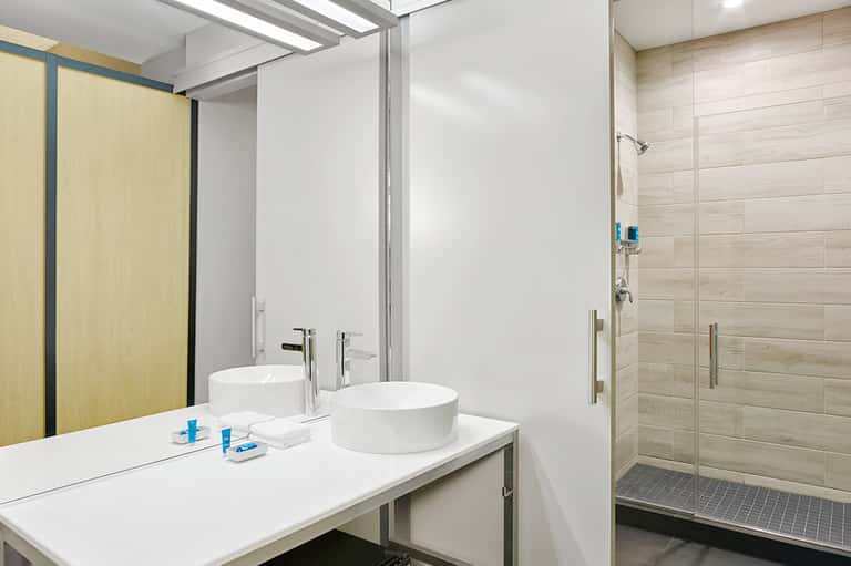 Contemporary bathroom with dual round sinks, white vanity, wooden accents, and walk-in shower