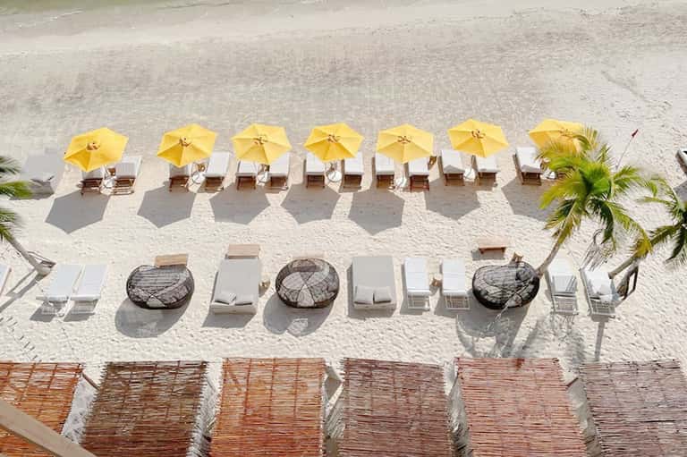 Aerial view of beach with six yellow umbrellas and lounge chairs arranged in rows on white sand