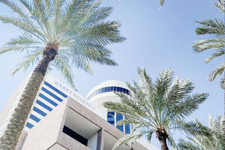 Modern Hyatt Regency hotel building with white architecture and palm trees against blue sky