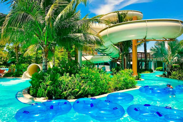 Tropical water park with turquoise pools, water slides, palm trees, and inflatable floats