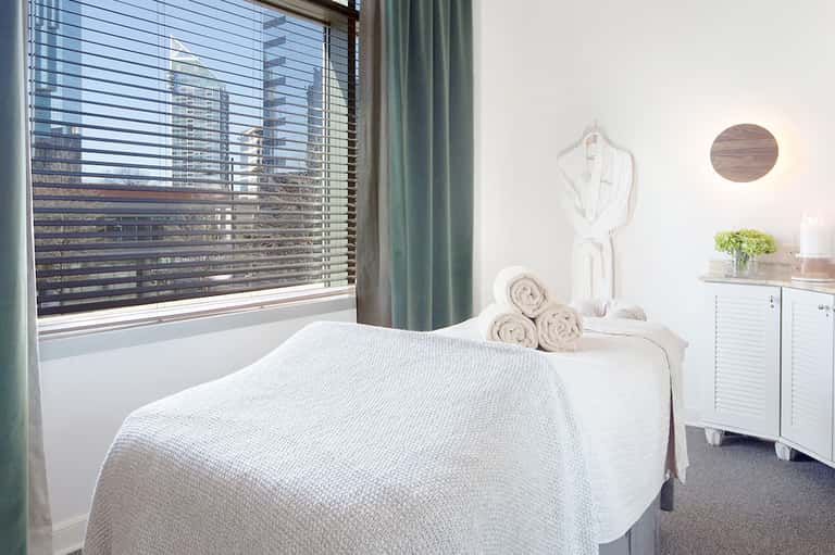 Spa treatment room with massage table, white linens, towels, and window with ocean view