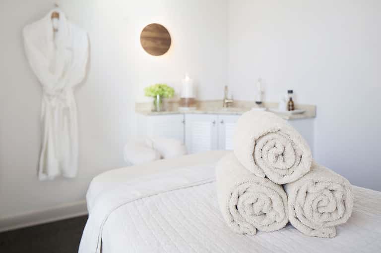 Minimalist spa bathroom with rolled white towels on bed and vanity sink