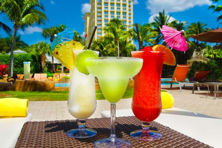 Three colorful tropical cocktails with fruit garnishes and decorative umbrellas on a poolside table