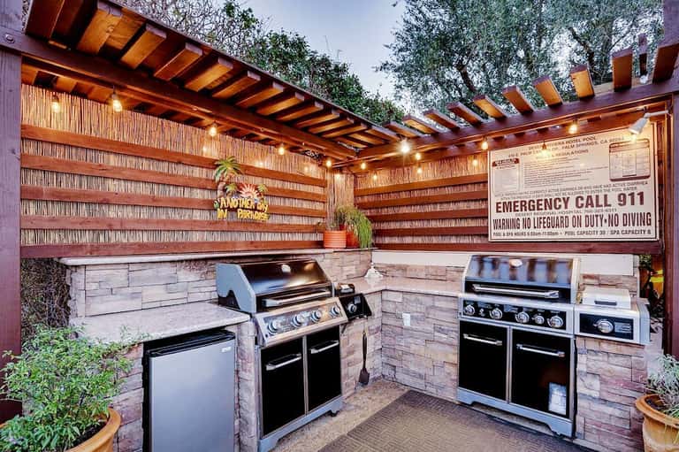 Covered outdoor kitchen area with multiple grills and brick walls under wooden pergola