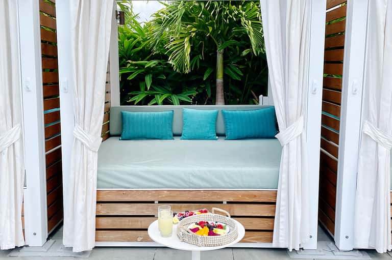 Luxurious daybed with turquoise pillows and white curtains in tropical setting