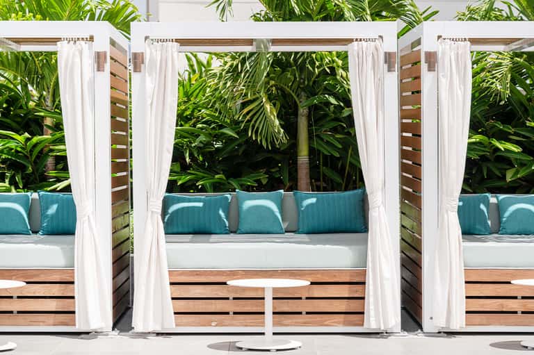White pergolas with flowing curtains and turquoise cushions in tropical garden setting
