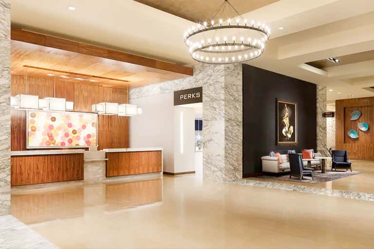 Upscale hotel lobby featuring marble columns, wooden reception desk, elegant chandelier, and contemporary seating area