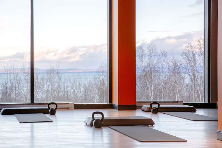 Modern fitness studio with kettlebells, yoga mats, and large windows overlooking winter landscape