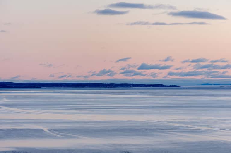 Serene coastal seascape at dusk with calm waters, distant shoreline, and pastel pink and blue sky