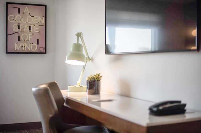 Minimalist office workspace with pale yellow desk lamp, potted plant, and neon pink wall art
