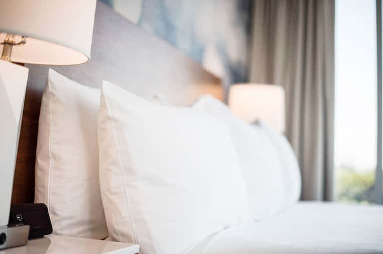 Luxury hotel bedroom with white pillows, bedside lamp, and curtains with ocean view