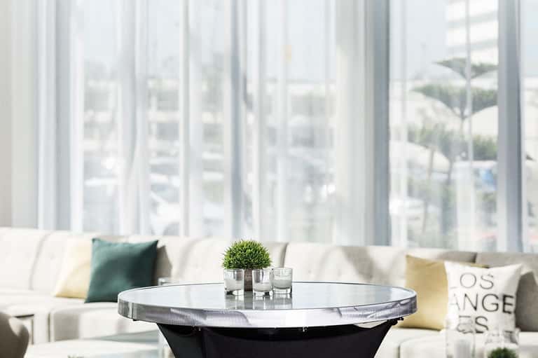 Minimalist lounge area with white sofa, round side table, and expansive windows overlooking palm trees