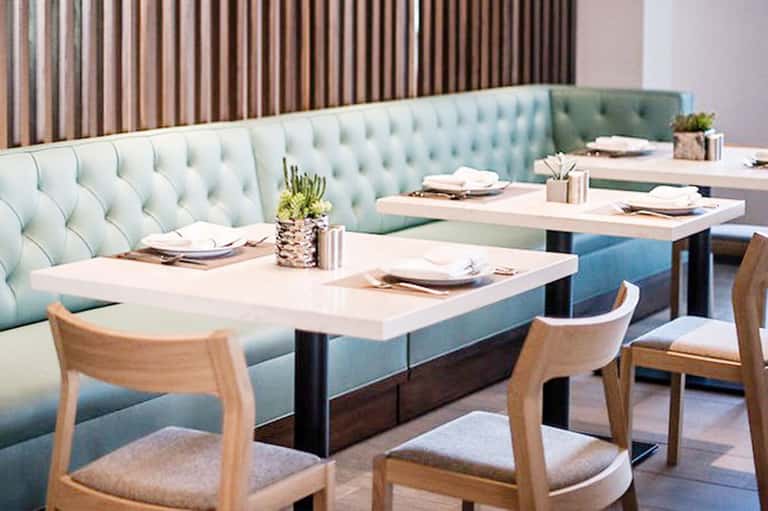 Modern restaurant dining area with mint green upholstered booths and wooden chairs