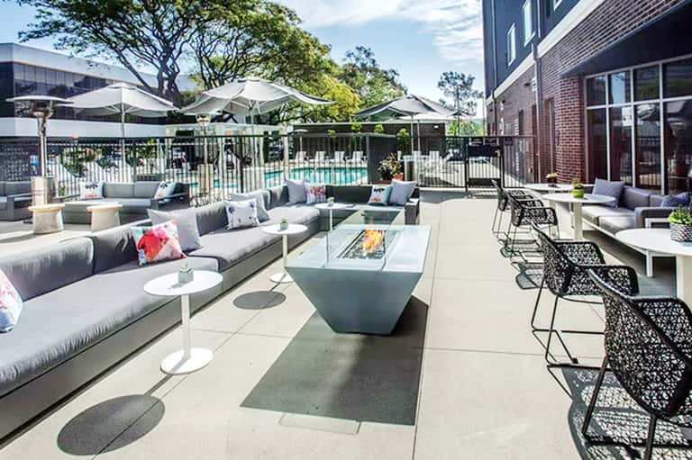 Modern outdoor terrace with gray sectional seating, fire pit, and metal chairs surrounded by landscaping