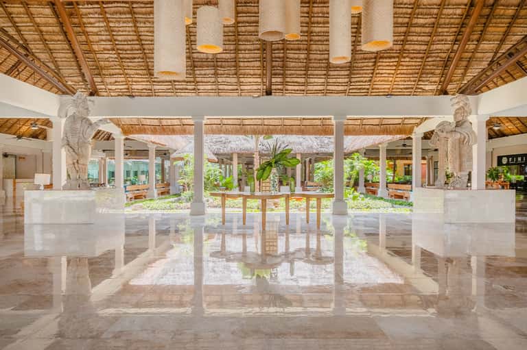 Modern spa lobby with polished marble floors, white columns, thatched ceiling details, and decorative statues