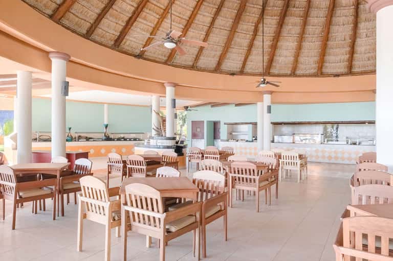 Beige and white dining area under thatched roof with round tables and wooden chairs