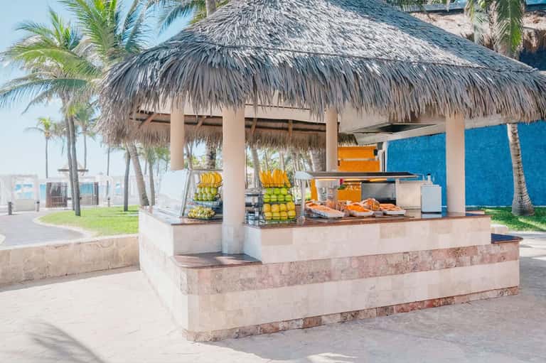 Beachfront fruit stand with thatched roof displaying oranges and grilled items