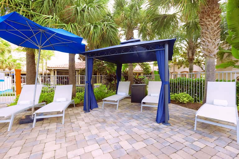 Blue pergola cabana with white lounge chairs under palm trees on paver patio