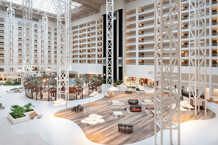 Modern hotel atrium with multi-story white framework, indoor pool, lounge seating, and decorative elements
