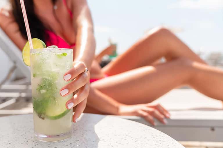 Woman holding mojito cocktail by pool with blurred resort background and sunny skies