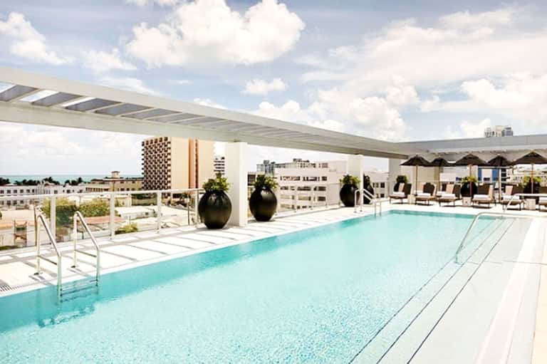 Modern rooftop swimming pool with turquoise water, lounge chairs, umbrellas, and city skyline views
