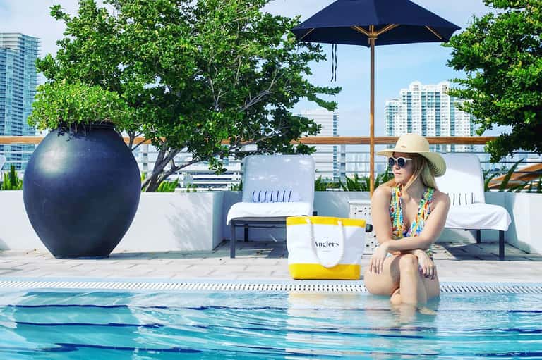 Woman in sun hat relaxing at hotel rooftop pool with city skyline views