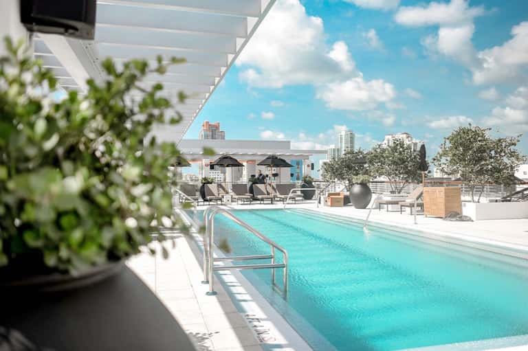 Rooftop pool with turquoise water, lounge chairs, umbrellas, and city skyline view on sunny day