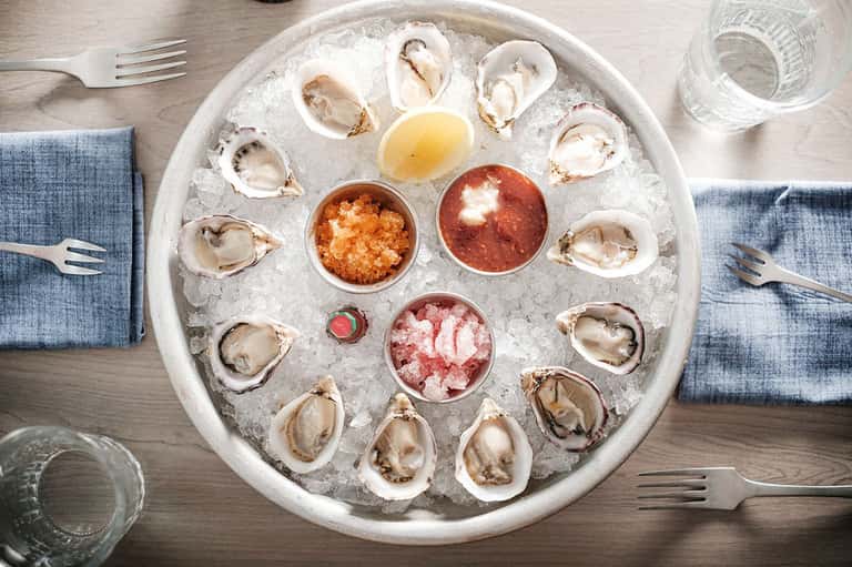 Oyster platter with ice and condiments on white plate with blue napkins