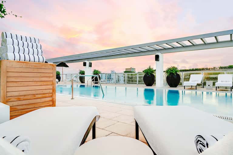 Modern rooftop pool with turquoise water, white loungers, and sunset sky at luxury hotel