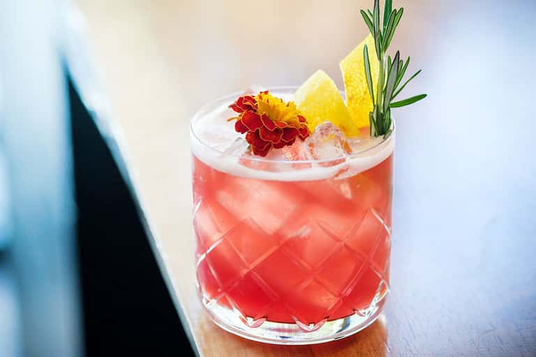 Tropical cocktail with red liquid, ice, pineapple, and flower garnish on wooden surface