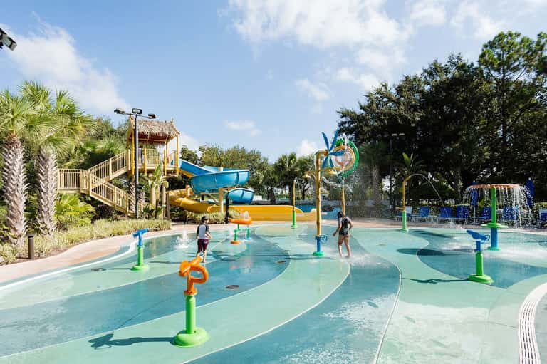 Colorful water park with splash pads, slides, palm trees, and children playing in shallow pools