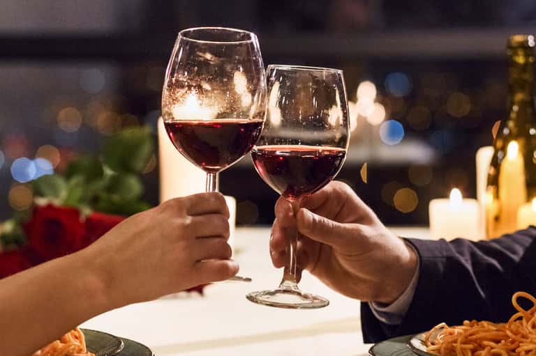 Two wine glasses clinking in a romantic dinner toast with candlelight