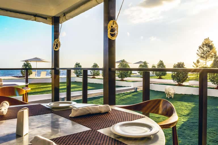 Waterfront dining setup with table settings, ocean view, and manicured green lawn with decorative elements