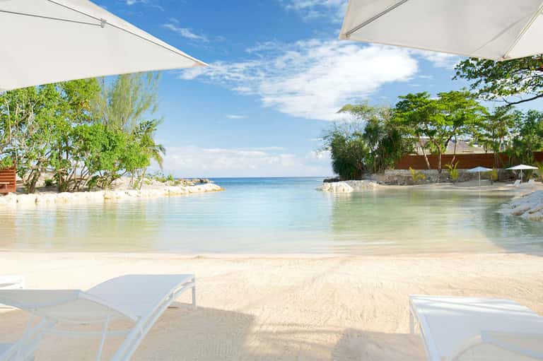 Pristine beach cove with white sand, turquoise water, and white umbrellas among tropical trees