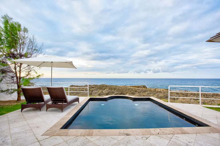 Modern oceanfront pool with lounge chairs and umbrellas overlooking rocky coastline