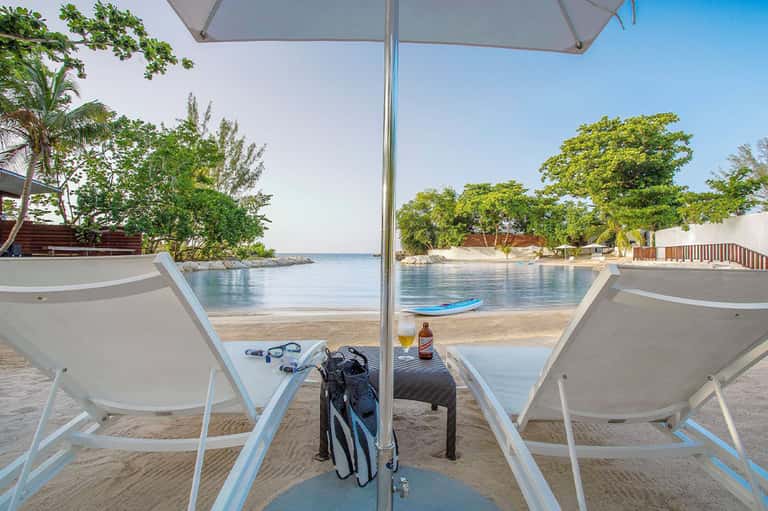 Beach loungers under umbrella with snorkeling gear and drinks overlooking calm lagoon