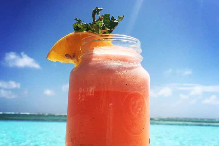 Tropical coral-colored frozen drink with fresh lime and mint leaves against bright blue ocean sky
