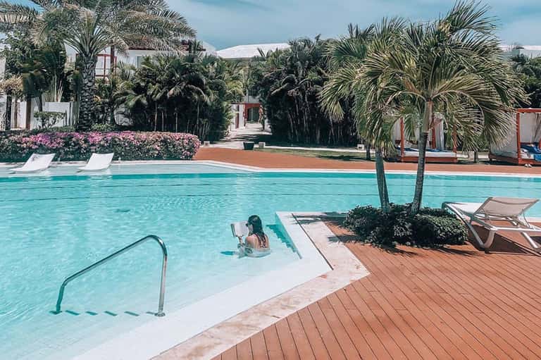 Turquoise resort pool with palm trees, lounge chairs, and mountain views