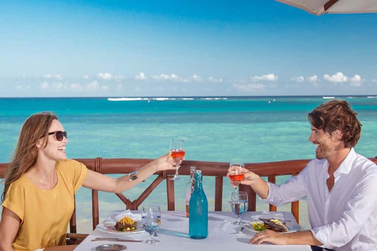 Couple toasting with glasses overlooking turquoise ocean from beachfront dining table