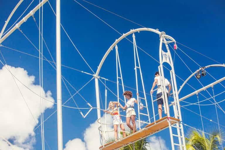 Guests enjoying a tall rope swing ride over tropical ocean under bright blue sky