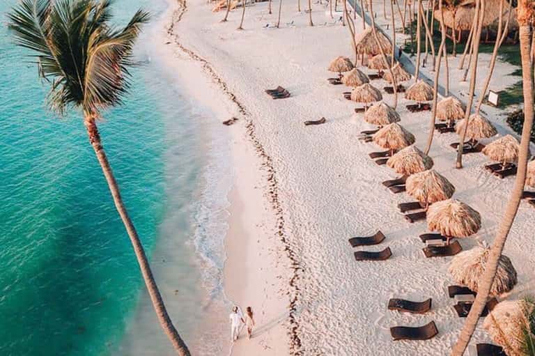 Pristine white sand beach with turquoise water, palm trees, and thatched umbrellas