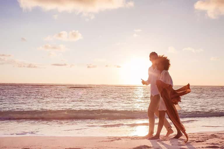 Couple running playfully on beach at sunset with ocean waves and golden sky