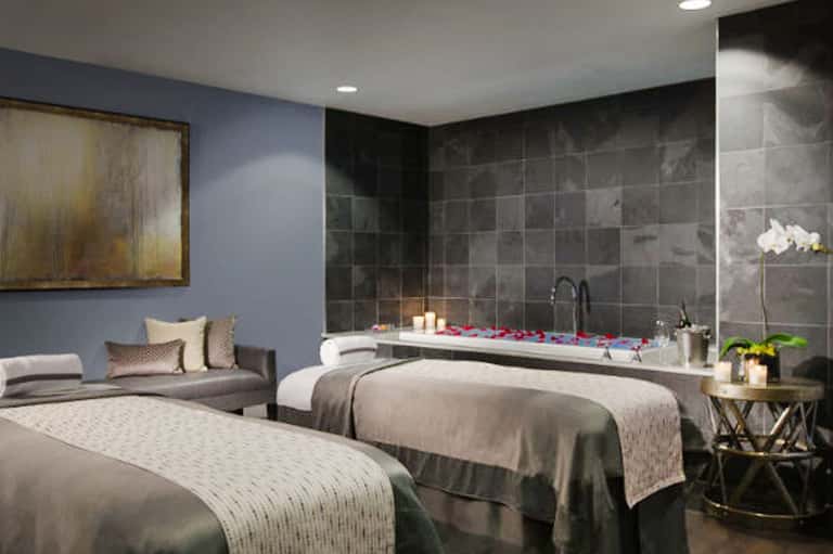 Luxury spa suite with two beds, soaking tub with candles, and relaxation seating area